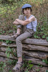 Portrait of a boy dressed in pants with suspenders and a sleeveless shirt, against a background of...