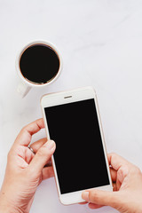 Hand holding smartphone with cup of black coffee on white marble background for media technology and modern lifestyles concept (Vertical image)