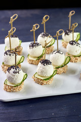 An unusual beautiful appetizing appetizer for a festive table. Mini canapes from a piece of baguette with sesame, thin slice of cucumber and a ball of cheese. Exotic black sesame for decoration.