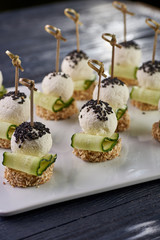 An unusual beautiful appetizing appetizer for a festive table. Mini canapes from a piece of baguette with sesame, thin slice of cucumber and a ball of cheese. Exotic black sesame for decoration.