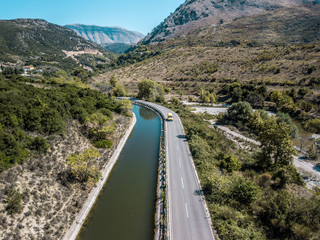 Aerial drone view of vehicle on road with mountains and river in background 