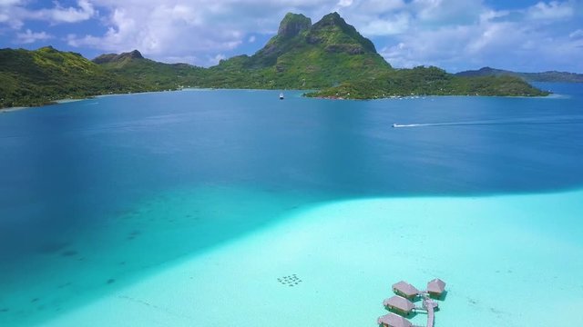 Aerial footage from a drone of luxury overwater villas with palm trees, blue lagoon, white sandy beach and Otemanu mountain at Bora Bora island, Tahiti, French Polynesia (Bora Bora Aerial)

