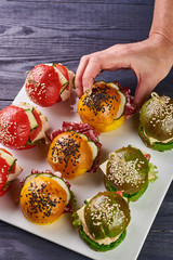 Fashionable set of multi-colored small hamburgers. Snack in the form of sandwiches with different fillings on a square plate. A treat for a buffet. Vegetarian and meat burgers.