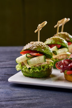 Fashionable set of multi-colored small hamburgers. Snack in the form of sandwiches with different fillings on a square plate. A treat for a buffet. Vegetarian and meat burgers.