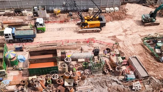 SINGAPORE - OCT 19, 2017: Top panoramic or aerial view of urban construction site with cranes unloading trucks and hard hat workers. Work of heavy equipment vehicles or machines. Time lapse