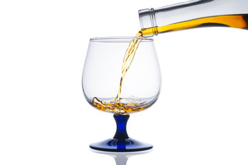Pouring cognac into glass from bottle on white background