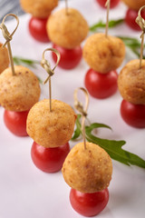 Appetizing and unusual snack for the festive table. A small treat on a skewer. A tiny round cutlet in breadcrumbs and a cherry tomato. Vegetarian snack with potato ball and tomato.