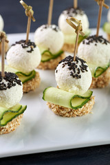 An unusual beautiful appetizing appetizer for a festive table. Mini canapes from a piece of baguette with sesame, thin slice of cucumber and a ball of cheese. Exotic black sesame for decoration.