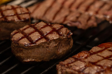 Three grilled beef tenderloin steaks coated bacon on grill