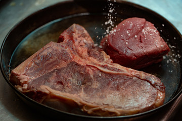 Raw T bone steak of beef meat in a frying pan against dark background. Selective focus.