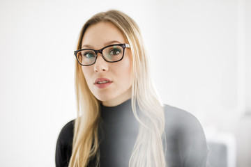 Junge blonde Frau mit Brille steht im hellen Raum