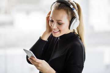 Junge Frau schaut auf ihr Handy und hört Musik mit ihren kabellosen Kopfhörer