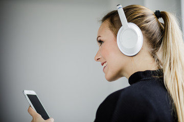 Junge Frau hält ihr Handy in der Hand und hört mit Kopfhörer Musik