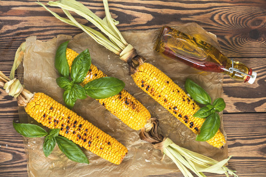 Corn baked in olive oil, with salt and basil on parchment paper on a dark surface