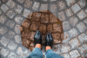 first person point of view woman step into puddle in black shoes