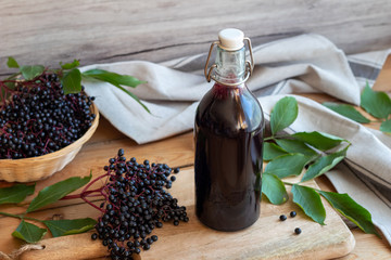 A bottle of black elder syrup with fresh elderberries