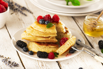 Pancakes with forest fruits berries on white table.