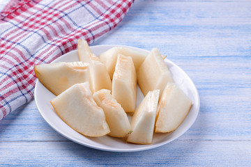 Pieces of fresh ripe melon on a white plate on a blue wooden table