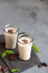 Delicious chocolate drink (milkshake, cocktail or smoothie) in glasses with pieces of chocolate on grey concrete background.