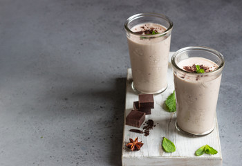 Delicious chocolate drink (milkshake, cocktail or smoothie) in glasses with pieces of chocolate on grey concrete background.