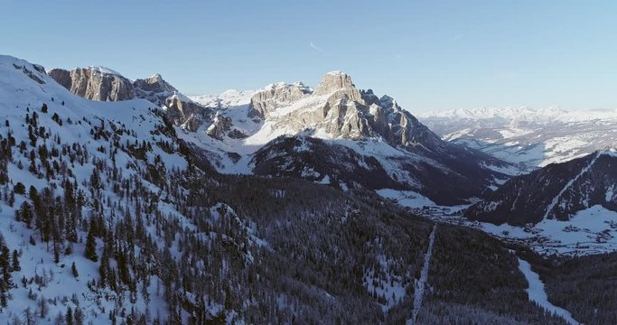 Backward aerial to snowy alpine valley with woods forest at Piz Boe.Sunny sunset or sunrise,clear sky.Winter Dolomites Italian Alps mountains outdoor nature establisher.4k drone flight