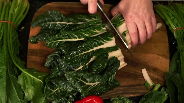 Woman's hands cut silverbeet spinach leaves on wooden cutting board in kitchen preparing healthy food