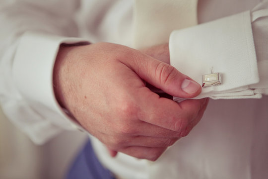 A man buttoning a cufflink on a white shirt