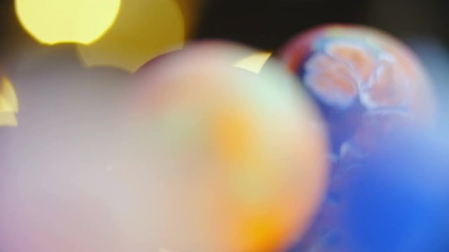 Slide over colorful marbles on glass surface macro shot 4K. Long shot dolly zoom-out with refocusing over colorful marbles and stopping at the single one.