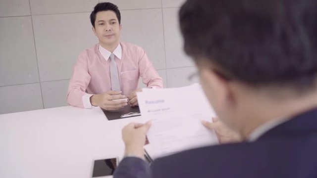 Slow motion - Attractive young Asian businessman in a job interview with corporate personnel manager who reading his CV. Asia businessman talking to male candidate at desk, interviewing job applicant.