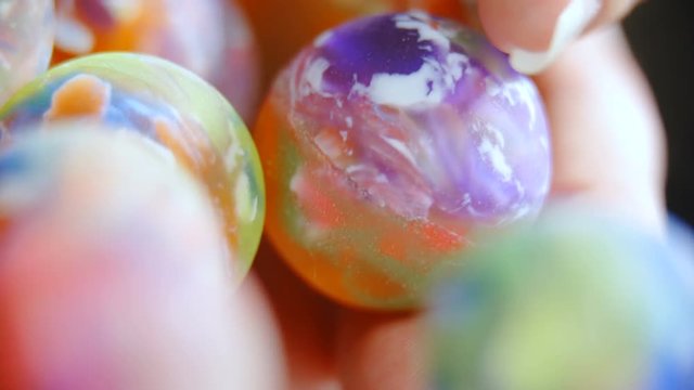 Colorful marbles roll off the person hands macro shot 4K. Long shot of a pile of marble balls in person's hand in focus while roll out of the frame.