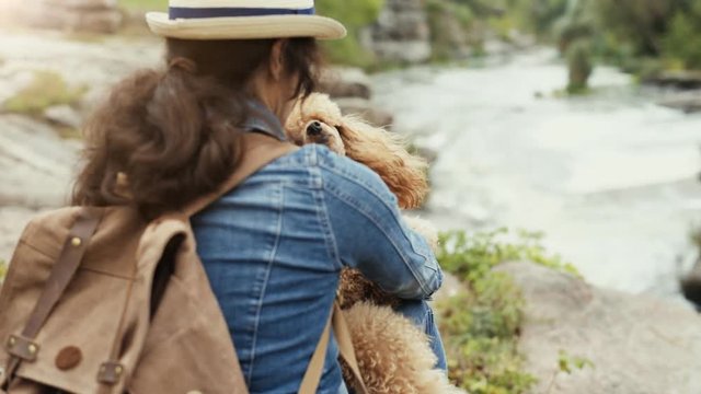 Woman traveler with backpack holding dog and looking at natural canyon with view of the mountain river.