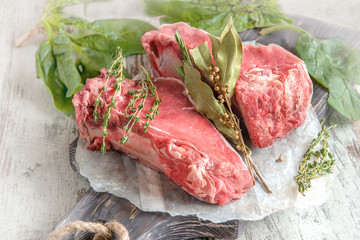 Cuts of beef for grilling on a wooden cutting Board with spinach, rosemary and Provencal herbs for the marinade in a rustic style