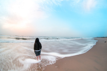 Woman standing at paradise beach in pondicherry watching the sunrise on a cloudy day. The sand surf...