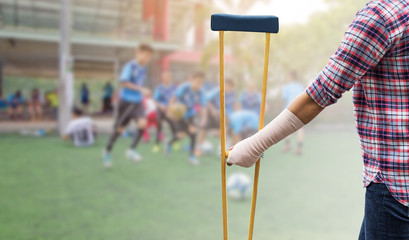 patient injured on arm and leg and hand holding wooden crutches isolated on blurred background kid soccer player in academy, insurance concept