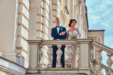 Beautiful newlyweds hugging while standing on the stairs of the beautiful old palace on a sunny day.
