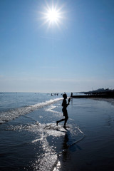 boy on the waters edge of Brighton beach on a hot sunny day the sun is star bursting  in the sky 
