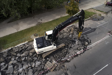 Excavator breaking concrete road surface with hydrohammer drill at repairing roadwork. Overhaul of the road, place of repair