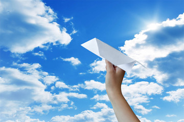 Hand of a man with a paper origami plane against the blue sky, the concept of a dream and the future