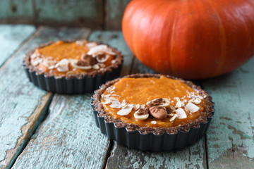 Healthy vegetarian dessert. Close up of open pumpkin pies in baking dish served with raw pumpkin on blue wooden background