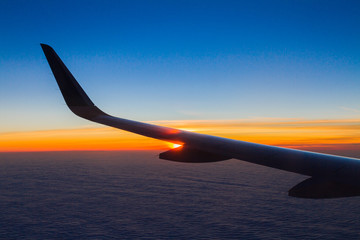 Blue planet Earth sky seen through an airplane window. Unique panoramic high altitude aerial view of a flaring tropical sunset in the cloudscape horizon behind the aircraft wing.