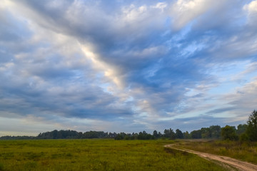 Road through fields and clouds to the sky