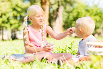 Smile. Cute pleasant girl smiling while feeding a small kid in the park