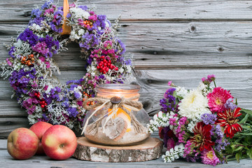 Bunte Herbstdekoration mit Blumenstrauß Äpfeln und Windlicht rustikal vor Holzhintergrund