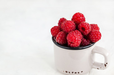 Fresh ripe raspberries in a mug on white