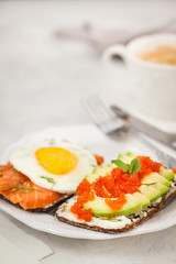 Avocado and red caviar, smoked salmon and fried egg rye toasts for breakfast, close up