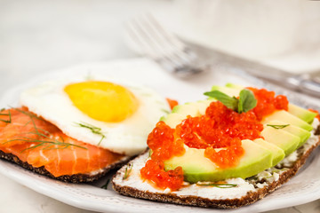Avocado and red caviar, smoked salmon and fried egg rye toasts for breakfast, close up