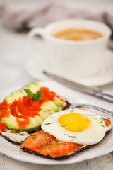 Avocado and red caviar, smoked salmon and fried egg rye toasts for breakfast, close up