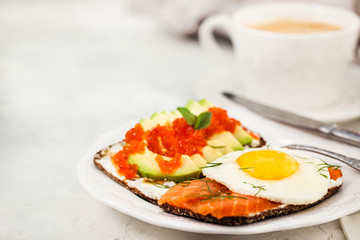 Avocado and red caviar, smoked salmon and fried egg rye toasts for breakfast, close up