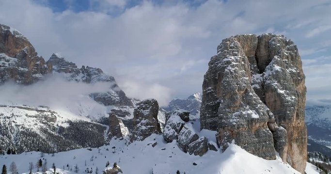 Backward aerial through majestic Cinque Torri rocky mounts. Sunny day with cloudy sky.Winter Dolomites Italian Alps mountains outdoor nature establisher.4k drone flight