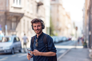 Portrait of young man listening music via headphones at urban street